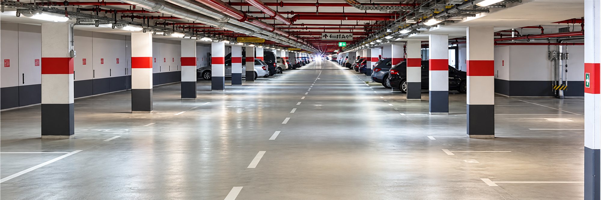 Parking souterrain bien éclairé, avec des piliers à bandes rouges et noires et des voitures garées